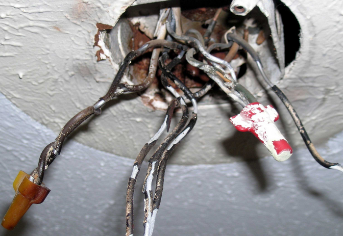 A tangled mess of electrical wires protrudes from a hole in a white wall, showing exposed connections with wire nuts.RetryClaude can make mistakes. Please double-check responses.
